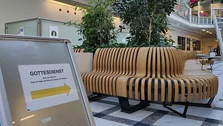 Sitzbank im Krankenhaus-Foyer, daneben Hinweisschild 'Gottesdienst'