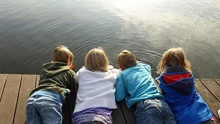 Vier Kinder liegen bäuchlings auf einem Steg am Wasser